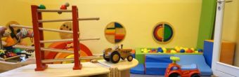 Zu sehen ist ein Spielzimmer. Genauer, eine Murmelbahn, ein Bobbycar, Puppen, ein Bällebad, Wandspiele und ein hölzerner Traktor.