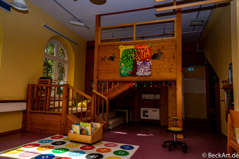 Gruppenraum mit Holzeinbauten, die weitere Räumlichkeiten schaffen. Spielzeug und ein buntes Jahreszeitenbild sind zu sehen.