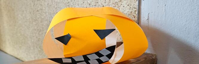 Gebastelter Kürbis aus orangefarbenen Papierstreifen mit Gesicht