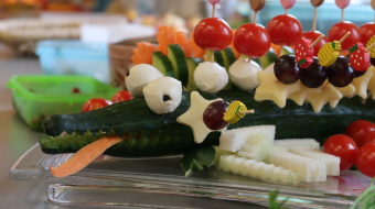 eine Gurke in Form eines Krokodils mit Tomate-Mozzarella-Spießen und Käse-Trauben-Spießen darauf